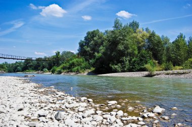 Öğleden sonra ağaçlar ve bir köprü ile bir beyaz taş shore bir arka plan üzerinde dağ nehir