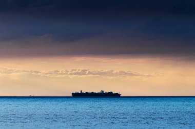 Kargo konteyner gemisi siluet Baltık Denizi dramatik karanlık nimbostratus bulut formasyonu altında geçiş ufukta. Gdansk defne, Polonya.