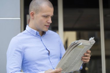 Yakışıklı ve olumlu bir işadamı portresi bina ve gazete okuma ofis önünde ayakta
