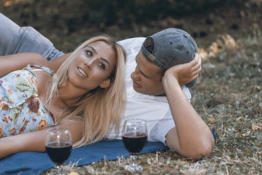 Having a büyük zaman, asma, bardak ile romantik genç çift adam kızı kucaklar. Onlar çim üzerinde yalan ve doğanın keyfini tadını çıkarın. Piknik