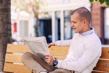 Şehrin bankta otururken yakışıklı bir genç adam portresi kapatın ve gazete okumak