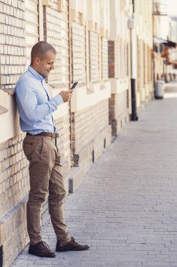 Bir cep telefonu kullanırken yakışıklı bir genç adam dışında portresi. Eski bina yanında duruyor. Manifatura mesaj. Kopya alanı