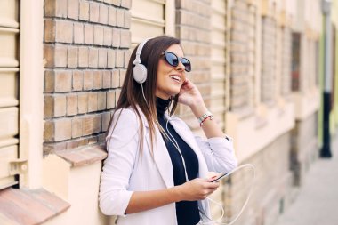 Güneşli bir günde sokakta kulaklık ile müzik dinlemek mutlu genç kadın