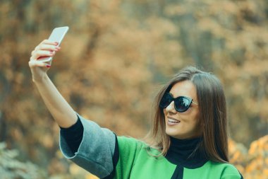 Güzel ve çekici bir genç kadın selfi cep telefonu ile doğada yapar. Harika bir sonbahar günü