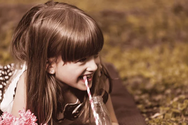 关闭小可爱的女孩躺在草地上的公园和喝果汁 — 图库照片