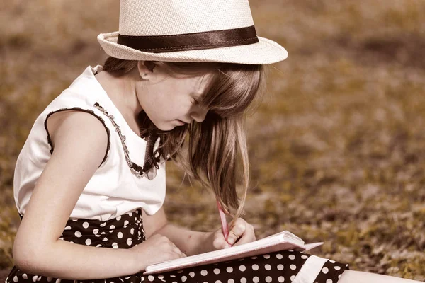 Menina Bonito Com Chapéu Vestido Senta Natureza Grama Escreve Desenha — Fotografia de Stock