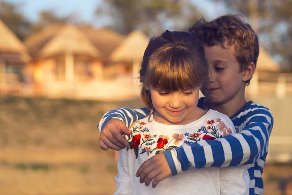 Kız ve erkek sahilde günbatımı anda oynamak. İlk aşkım. Göl kenarında oturup iyi vakit geçirin. Güzel bir kız sarılma küçük şirin çocuk. Hatırlamak harika anlar
