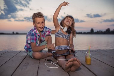 Olumlu çocuklar dijital tablet ahşap iskele üzerinde birlikte ile oynarken portresi. Eğleniyor, gülüyor, güzel gün batımını zevk çocuklar