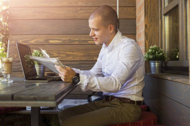 Bir kafede otururken, gazete okuma ve sabah kahve içme girişimci genç adam. Onun önünde bir dizüstü bilgisayar var