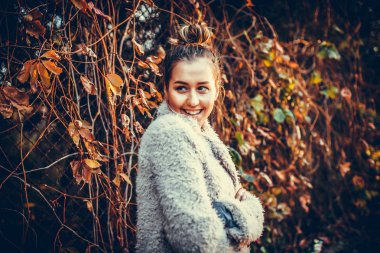Sonbahar yaprakları arka planda eski demir çit ile çevrili genç güzel gülümseyen kız