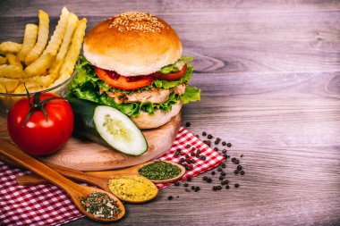 Lezzetli ev yapımı tavuk burger patates, taze marul, domates, salatalık, turp ve baharat rustik ahşap zemin ile hazırlanıyor. Kopya alanı