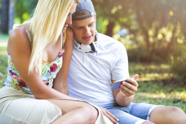 Genç çift web sörf / cep telefonu fotoğraflarına bakmaktan. Cute, gençler, adam ve eğlenmek için akıllı telefon kullanan kız