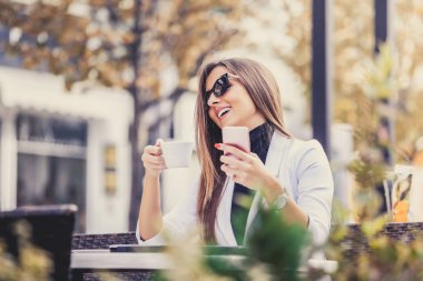 Mutlu girişimci bir telefon ve dizüstü bilgisayar ile ve sokağın ortasında bir kafede kahve içme. Kız sohbet, internet, bloglama tarama.