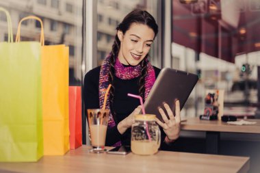 Mutlu genç kadın kahve içme / limonata ve tablet bilgisayara bir kahve dükkanında alışveriş sonra kullanarak. Seçici odak ve küçük alan derinliği.