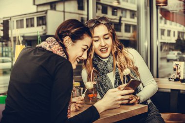  İki kafede kahve yudumlarken smartphone kullanarak gülümseyen kız güzel. Dostluk ve teknoloji.