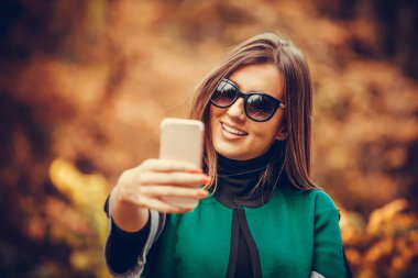 Güzel ve çekici bir genç kadın selfie cep telefonu ile doğada yapar. Harika bir sonbahar günü