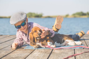 Nehir kenarında köpeğiyle yalan küçük şirin çocuk. Birlikte güzel güneşli bir günde hoşlarına gidiyor. Çocuk onun köpek yavrusu sarılma. Ben büyürken, hayvanlar - köpek, boş zaman, seyahat, tatil için seviyorum. Kopya alanı