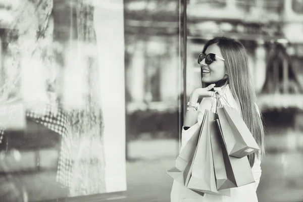 ショッピング センターでの買い物袋で美しく 幸せな若い女性 買い物をしている女性 お店のウィンドウを見ている女の子 黒と白の写真 — ストック写真