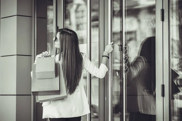 Happy young woman with shopping bags entering shop. Happy woman going into a store. Black and white photo