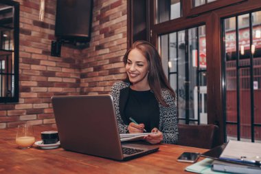 Girişimci bir dizüstü bilgisayar ve bir defter kafede Not almak online çalışma.