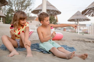 Kumlu sahilde oturan ve dondurma yemek mutlu pozitif çocuklar. İnsanlar, çocuk, arkadaş ve dostluk kavramı