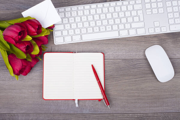 Wooden desk with a keyboard, mouse and notes, pen and tulips  from above