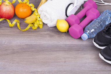 Fitness kavramı ile bir şişe su, bir cep telefonu ve kulaklık, ağırlıklar, havlu, elma ve ahşap arka plan üzerinde spor ayakkabı