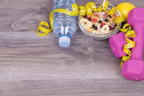 Fitness concept with bottle of water, muesli and fruit on a wooden background