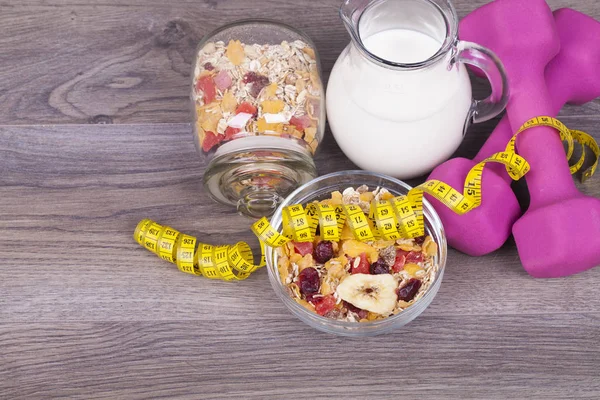 Fitness concept with weights, yoghurt, muesli and fruit on a wooden background