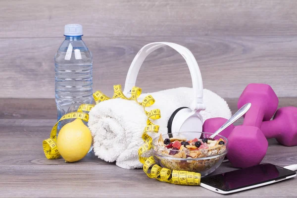 Fitness concept with a bottle of water, a mobile phone and headset, weights,towel, muesli, lemon and sneakers on a wooden background.With empty space for your text
