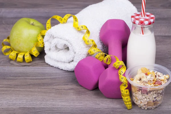 Fitness concept with yogurt to kefir,muesli, apple, weight and towel  on a wooden background . With empty space for your text.
