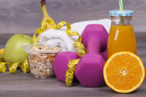 Fitness concept with weights, a towel, muesli, apple, orange and fresh squeezed orange juice.
