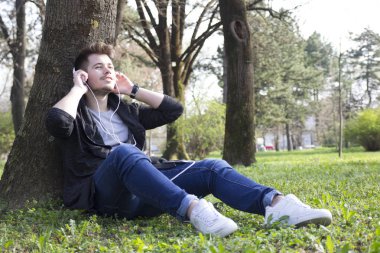 Yakışıklı genç çimlerde oturan adam ve müzik sahiptir. Seçici odak ve küçük alan derinliği.