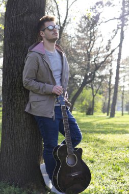 Parkta bir gitarla zevk yakışıklı delikanlı. Seçici odak ve küçük alan derinliği.