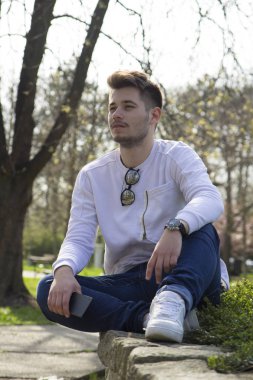 Yakışıklı genç adam oturur ve açık havada sahiptir. Seçici odak ve küçük alan derinliği.