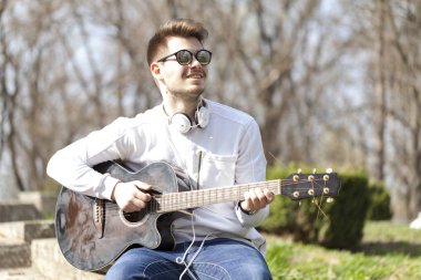 Parkta bir gitarla zevk yakışıklı delikanlı. Seçici odak ve küçük alan derinliği.