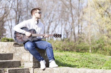 Parkta bir gitarla zevk yakışıklı delikanlı. Seçici odak ve küçük alan derinliği.