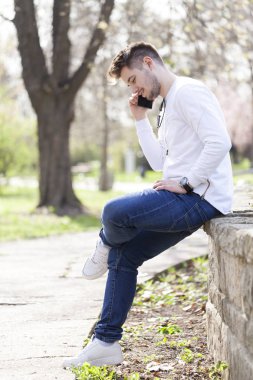 Yakışıklı genç adam telefon ederek ve açık havada sahiptir. Seçici odak ve küçük alan derinliği.
