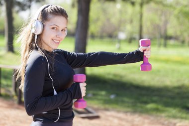 Parkta ağırlıkları ile egzersiz yaparak güzel ve genç birbayan. Seçici odak ve küçük alan derinliği.
