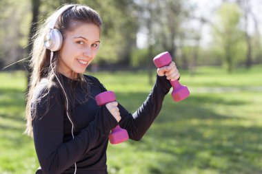 Parkta ağırlıkları ile egzersiz yaparak güzel ve genç birbayan. Seçici odak ve küçük alan derinliği.