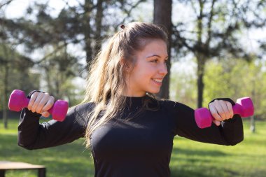 Parkta ağırlıkları ile egzersiz yaparak güzel ve genç birbayan. Seçici odak ve küçük alan derinliği.