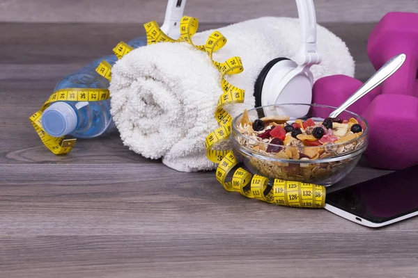 Fitness concept with a bottle of water, a mobile phone and headset, weights,towel and muesli on a wooden background