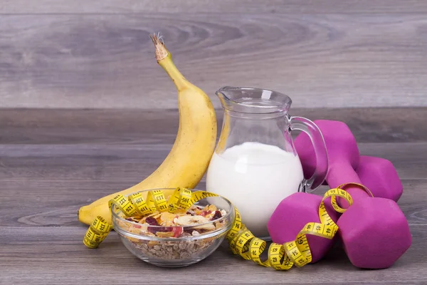 Fitness and diet concept with  weights,yoghurt, muesli and banana on a wooden background