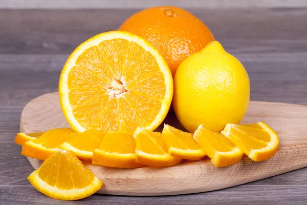 Fresh and juicy orange cut into pieces and lemon on a wooden background
