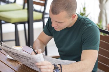 Genç adam dikkatle okuma gazete reklamları ve arama Daire Kiralık bir masada oturur