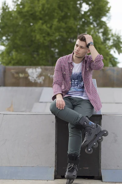 Handsome young man with roller skates sitting and resting