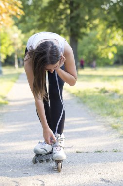 Genç güzel kadın tekerlekli paten üzerinde ride ve kazaları önlemek için onun Ayakkabı bağcıklarımı bağlayacak bıraktı