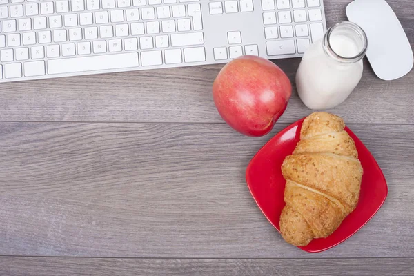 Work desk with keypad and breakfast. Keyboard on the desk, croissant, yogurt and apples. Pausing during working hours. Top view.With empty space for your text