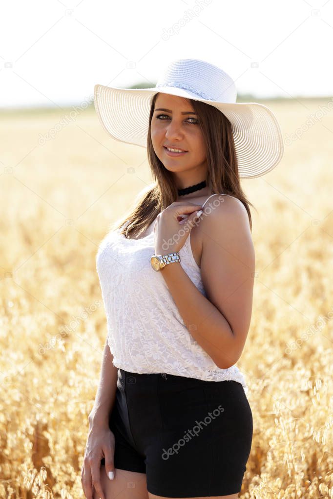 Close up portrait of a beautiful young woman with hat and blurred wheat field and sky on background
