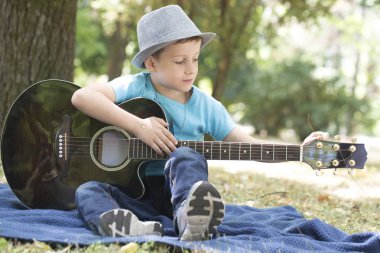 Çim ve gitar çalmak şapkalı küçük şirin küçük çocuk. O çok müzikal ve gitar çalmayı öğrenmek çok kolay. O gerçekten hoşlanıyor.